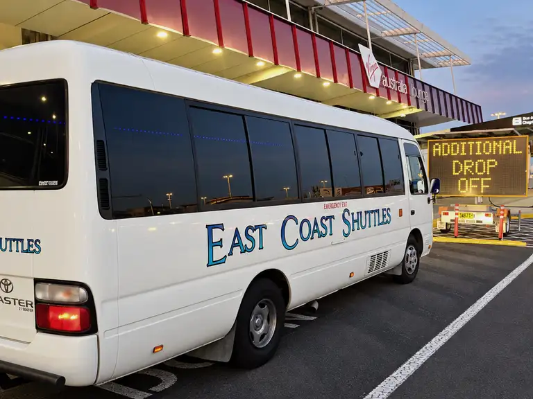 White Toyota Coaster with East Coast Shuttles lettering at an airport drop-off.